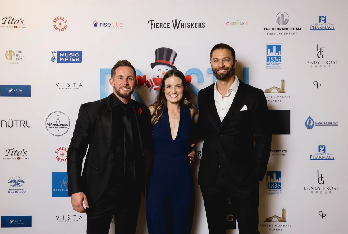Frosty Gives Back hosts in black tie at the step and repeat, with Frosty the snowman and sponsor logos behind them