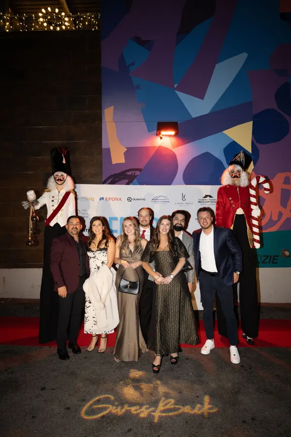 Guests on the red carpet with nutcracker stilt walkers and "Gives Back" lit up on the ground