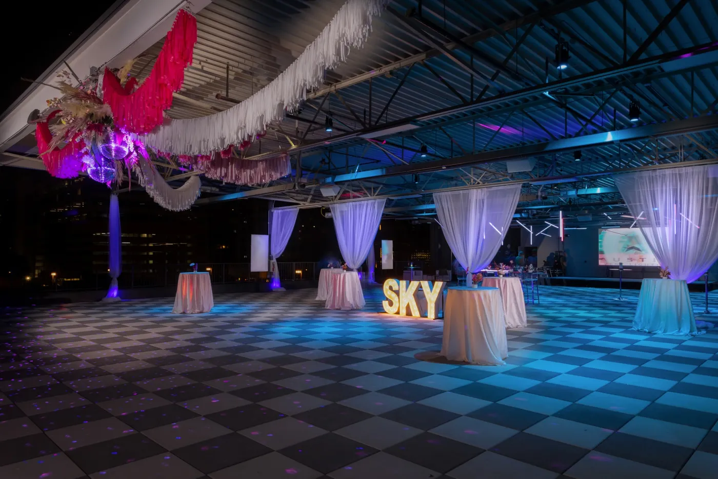 The SKYBOX on 6th event space at night: checkered dance floor, draped cocktail tables and lighted SKY letters